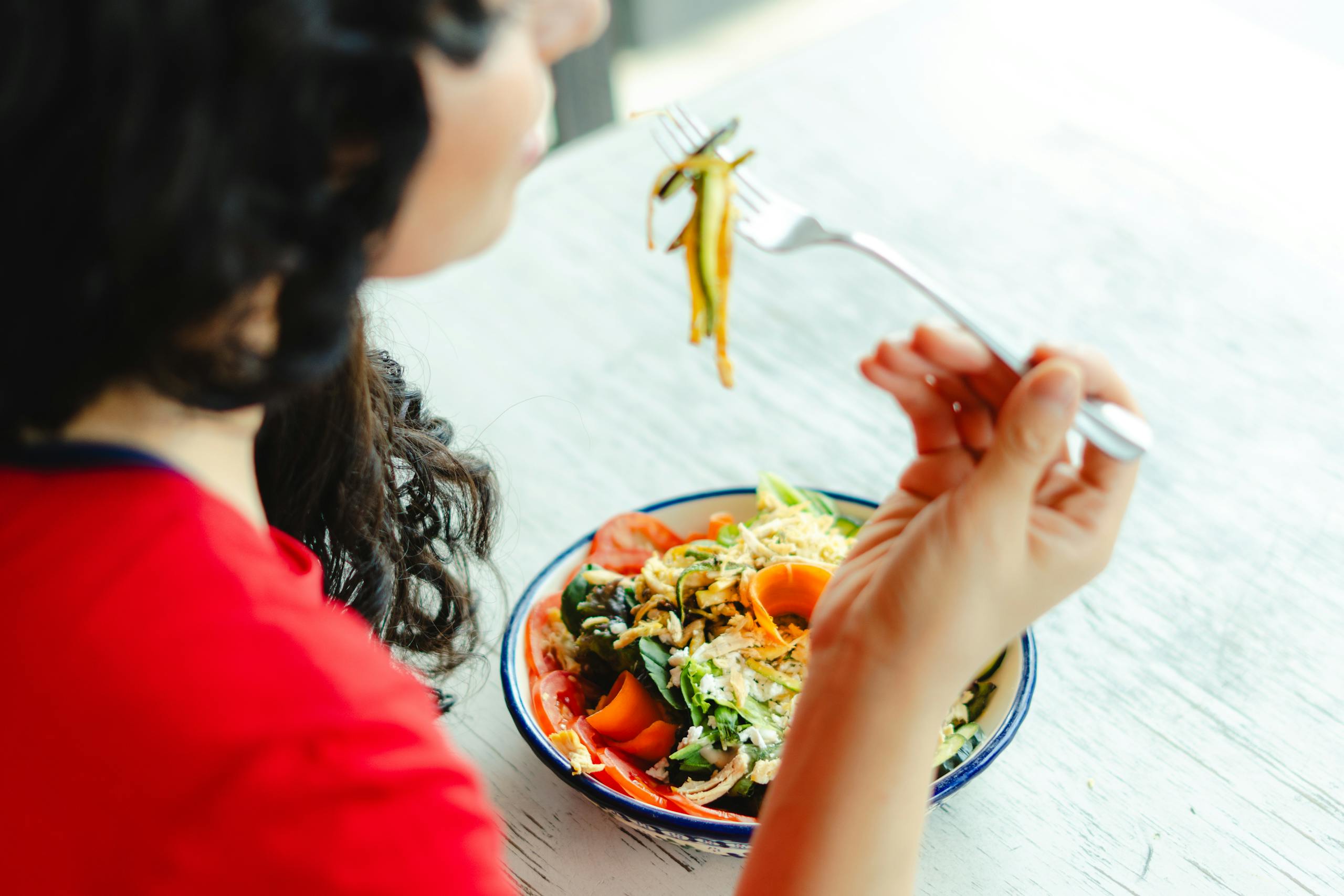 What I Wish I Knew Before Starting GLP-1 — A Dietitian's Honest Answer woman in a red shirt enjoys a fresh salad indoors at a restaurant table.